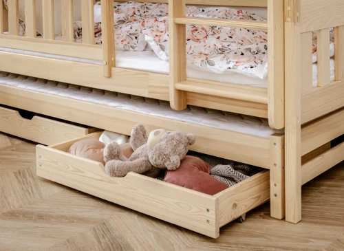 Åben udtræksskuffe under en træseng med en bamse, puder og tøj til opbevaring.