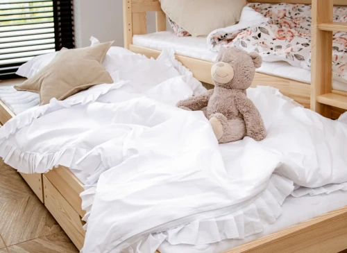 Bamse på hvidt sengetøj i nederste køje af trækøjeseng