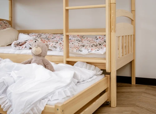 Køjeseng i lyst træ med stige. Nedre seng med hvidt sengetøj og bamse, øvre seng med mønstret sengetøj.