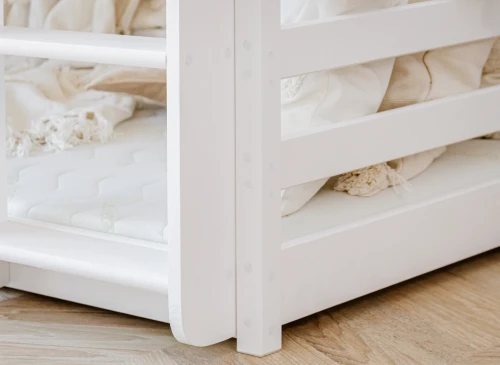 Underseng på hvid tredobbelt køjeseng med madras, lyse tekstiler og indbygget reol.