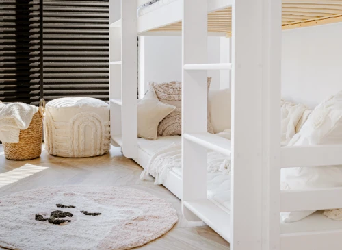 Nederste del af hvid trippel køjeseng, med gulvtæppe og puf i et lyst børneværelse.