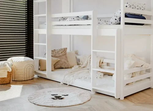 Hvid trippel køjeseng i lyst værelse med sødt tæppe, puf og sorte persienner.