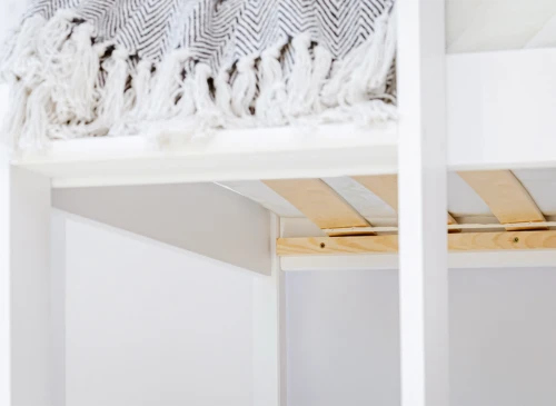 Nærbillede af hvid køjeseng med gråt tæppe og trælameller