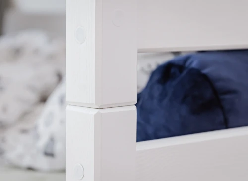 Nærbillede af hvid køjesengsramme med blå pude i baggrunden.