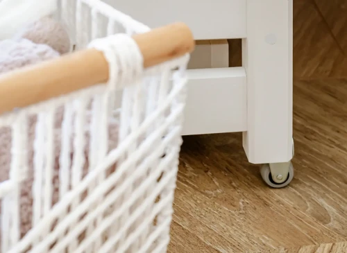 Detalje af udtrækssengens hjul for nem bevægelse og hvid flettet opbevaringskurv til legetøj.