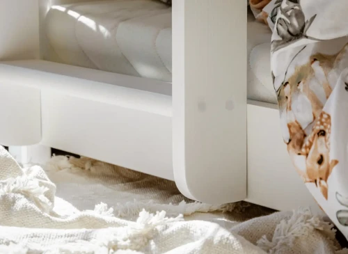 Detalje af den hvide sengeramme i træ med glat finish og sengetøj med dyremotiv. Holdbar konstruktion.