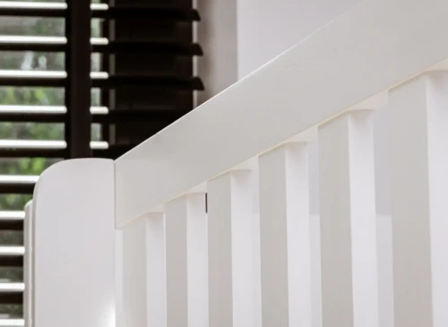 Nærbillede af hvidtremmet tremmeseng i træ med lameller, der reflekterer sollyset blidt.