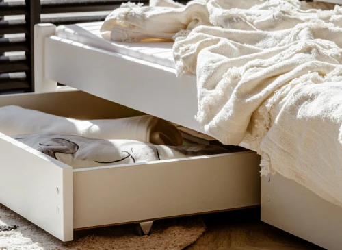 Udtræksskuffe under seng med opbevaring af sengetøj, en blød hvid plaid ligger på den øverste madras.