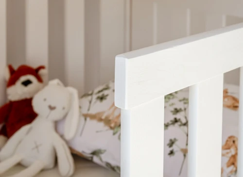 Detalje af hvid tremmeseng med bamser og mønstret sengetøj, klar til babyens søvn og leg.