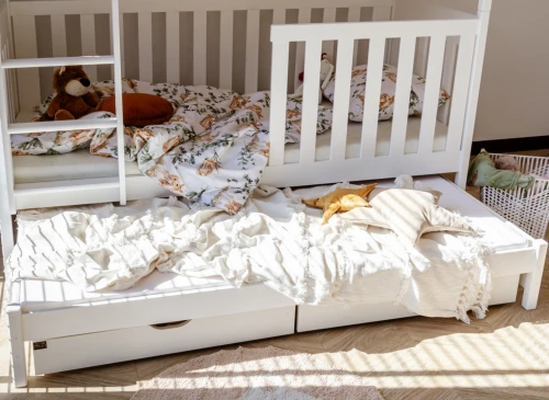 Hvid køjeseng med udtræksseng dækket af tæpper og puder, med legetøj og en kurv til opbevaring.