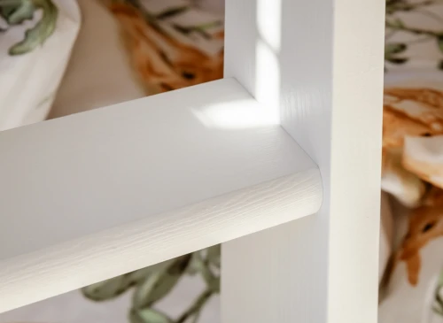 Nærbillede af trin på hvid træstige til køjeseng, med synlig træstruktur og blødt sollys.