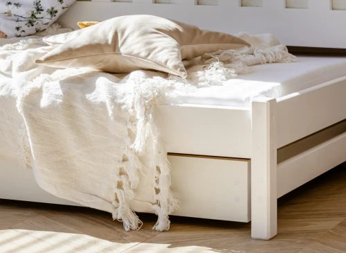 Udtræksseng med hvidt tæppe og stjerneformet pude, integrerede opbevaringsskuffer under sengen.