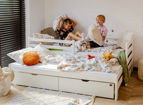 To drenge leger med puder på en hvid udtræksdaybed i et solrigt værelse.