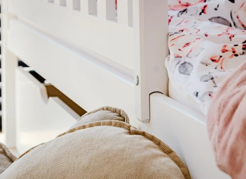 Nærbillede af hvid tremmesengs sengehest og beige pude, detalje af robust konstruktion.