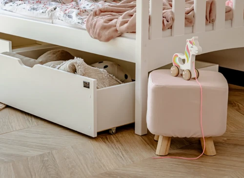 Hvid børneseng med åben skuffe til opbevaring under sengen. Ved siden af en pink skammel og træenhjørning.