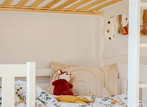 Nærbillede af nederste køje med regnbuepude og rød rævebamse i et hyggeligt børneværelse.
