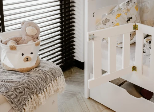 Hvid køjeseng med åbent sikkerhedsgitter ved siden af opbevaringskasse med bamse.