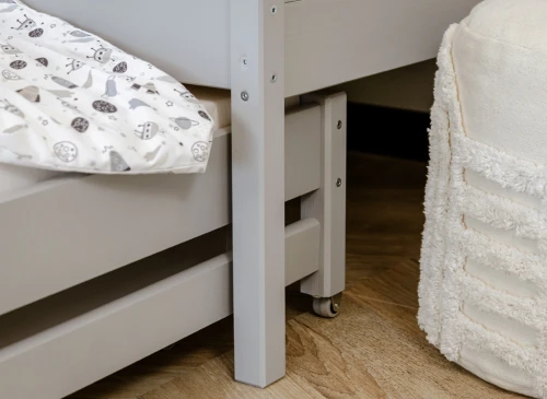Nærbillede af gråt sengeben og hjul på udtrækssengen ved siden af en hvid puf.