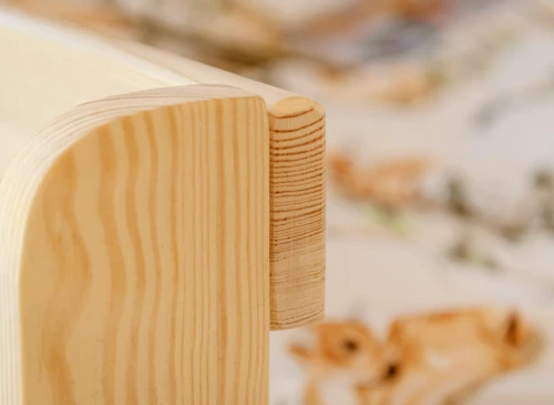 Nærbillede af afrundet samling på træsengsramme med synlig årestruktur i lyst træ.