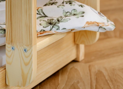 Detalje af robust træseng med afrundede hjørner og en mønstret pude. Bæredygtigt fyrretræ.