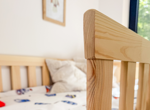 Detalje af trærammen på en juniorseng, med rumtema sengetøj i baggrunden, understreger kvalitet.