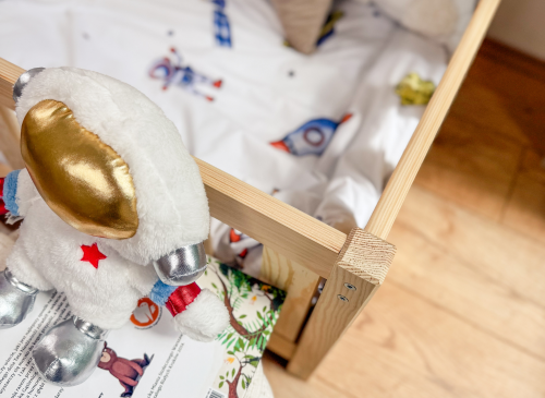 Astronaut bamse på bøger ved siden af en træ juniorseng med rumtema sengetøj, klar til eventyr.