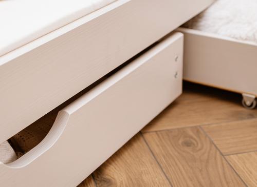 Nærbillede af sengens ramme og udtræksskuffe med udskåret håndtag og hjul. Praktisk opbevaring.