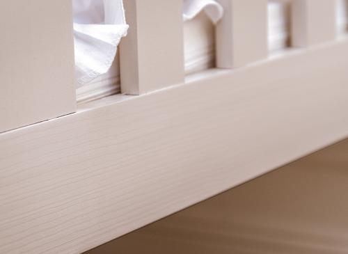 Nærbillede af sengehest i lyst træ og hvidt sengetøj. Kvalitetsdetaljer på en børneseng.