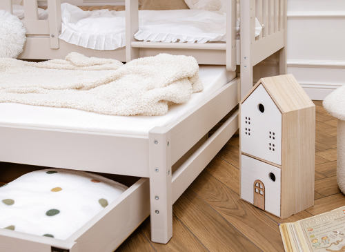 Underste køjeseng med åben udtræksseng til ekstra madras eller opbevaring, ved siden af et legetøjshus.