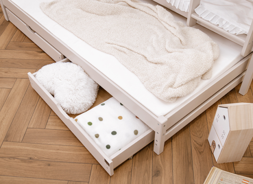 Åben udtræksseng skuffe under en køjeseng, fyldt med tæpper og en hvid plysset pude, smart opbevaring.