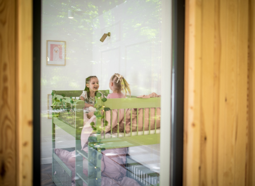 To glade piger leger i en grøn køjeseng, set gennem vinduet. Børneværelse med stilfuldt design.