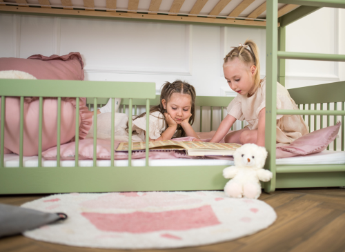 Piger læser en bog i den nederste køje af en grøn seng. Ro og fordybelse på et børneværelse.