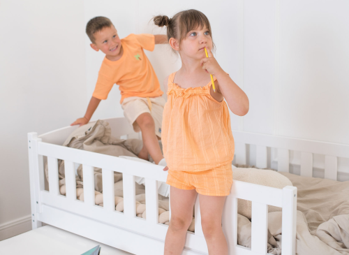 Hvid børne daybed med to legende børn; en pige foran og en dreng på sengen.