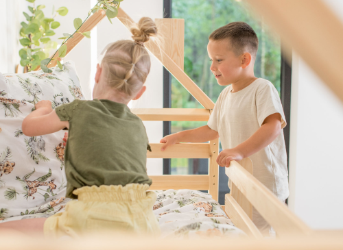 To børn leger i den nederste køje i en hus-køjeseng i træ.