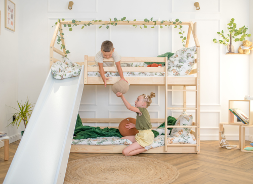 Børn leger med pude på en træ-køjeseng med rutsjebane. Børneleg i hyggelig seng med grønt sengetøj.