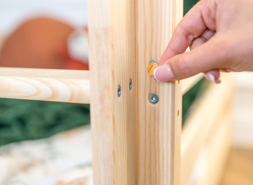 Nærbillede af hånd der sætter træprop i skruehul på køjesengens træramme.