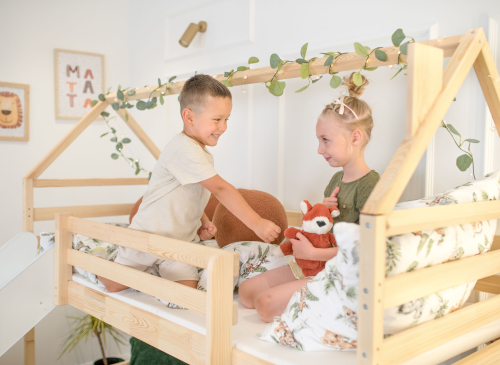 To børn leger i en køjeseng formet som et hus med grønne slyngplanter.