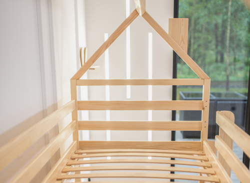 Tom køjeseng i træ med husramme og lamelbund i et børneværelse.