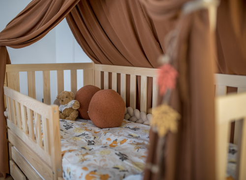 Hyggelig træ juniorseng med brun sengehimmel, bamse og mønstret sengetøj i børneværelse.