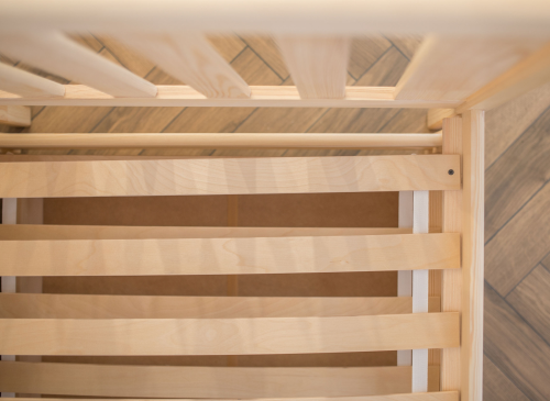 Nærbillede af trælameller til børneseng, der viser sengeramme og gulv i trælook.