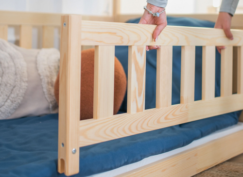 Nærbillede af hånd der monterer en træ-sikkerhedsbarriere på en hus-tremmeseng i naturtræ.