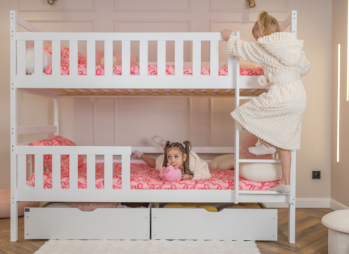 To piger leger og klatrer i en hvid køjeseng med stige og skuffer.