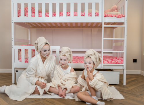 Mor og døtre med ansigtsmasker og badekåber foran en hvid køjeseng.