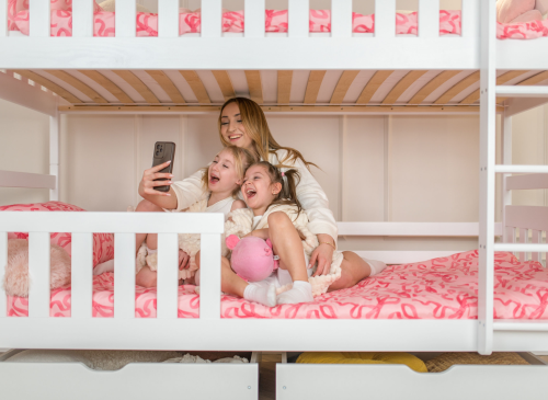 Glad mor og døtre tager en selfie i en hvid køjeseng.