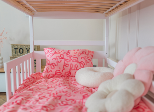 Lyserødt sengetøj med sløjfemønster og hvide puder i en børneseng.