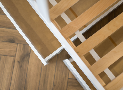 Nærbillede af hvid sengeramme med trælameller og opbevaringsskuffe under sengen.